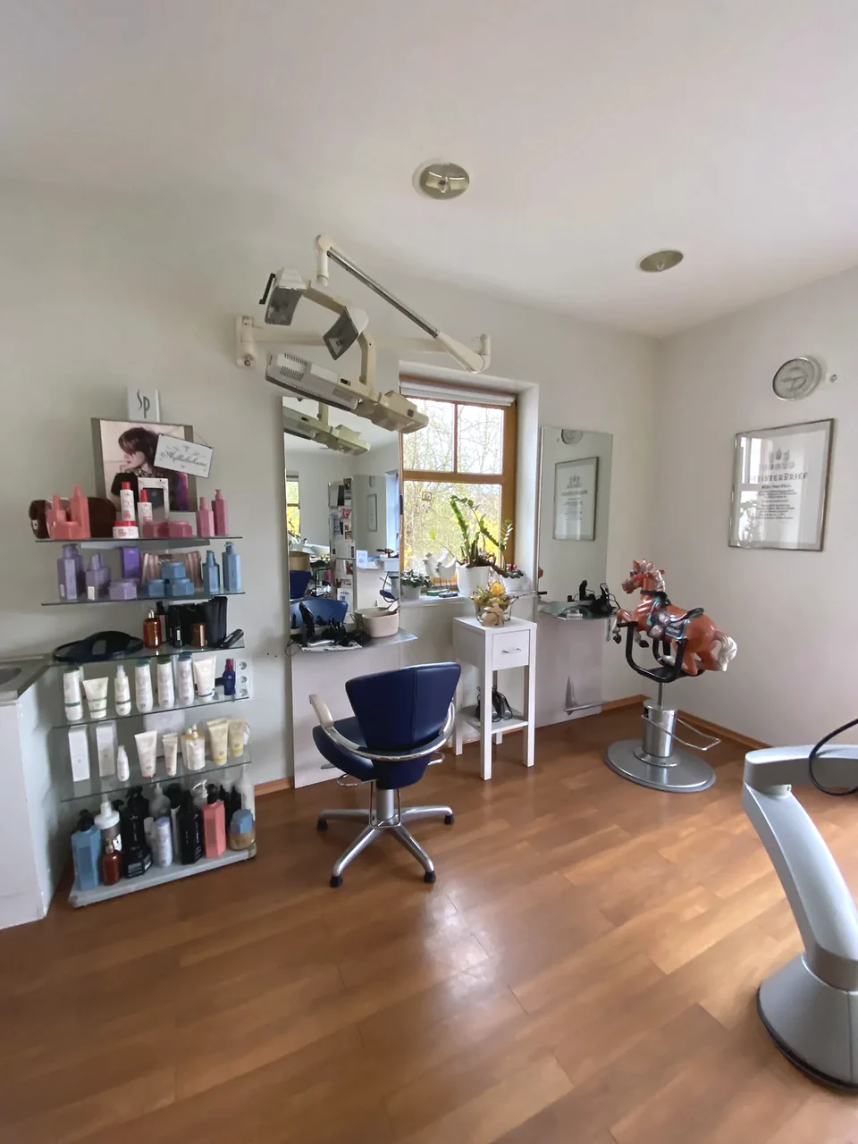 Salonraum mit Spiegel, Fenster und blauem Frisierstuhl