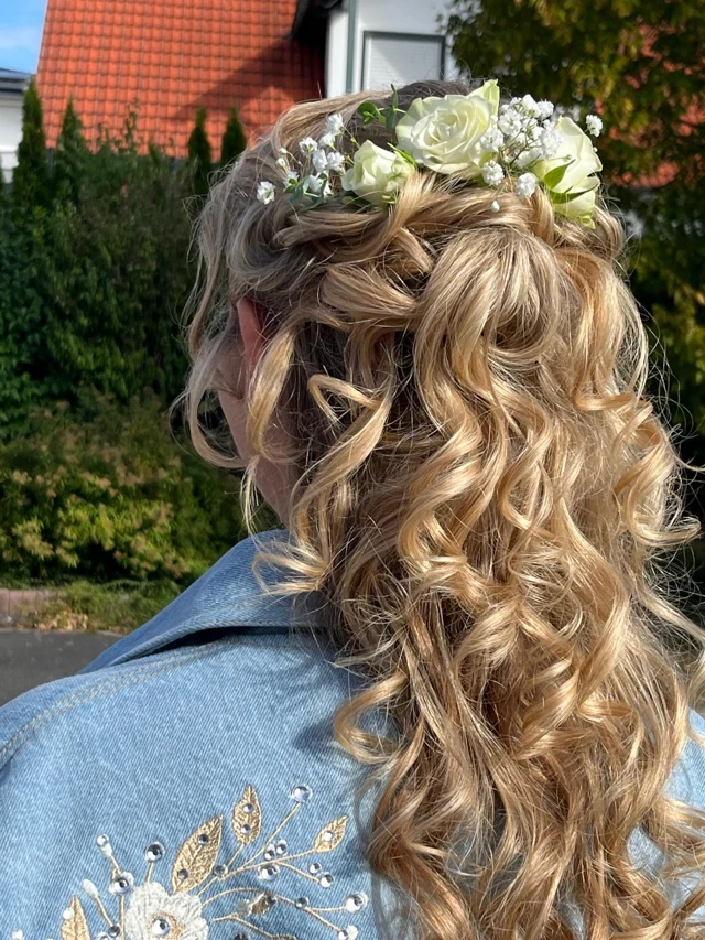 Halb hochgesteckte blonde Locken mit weißen Rosen und kleinen weißen Blüten in der Rückansicht